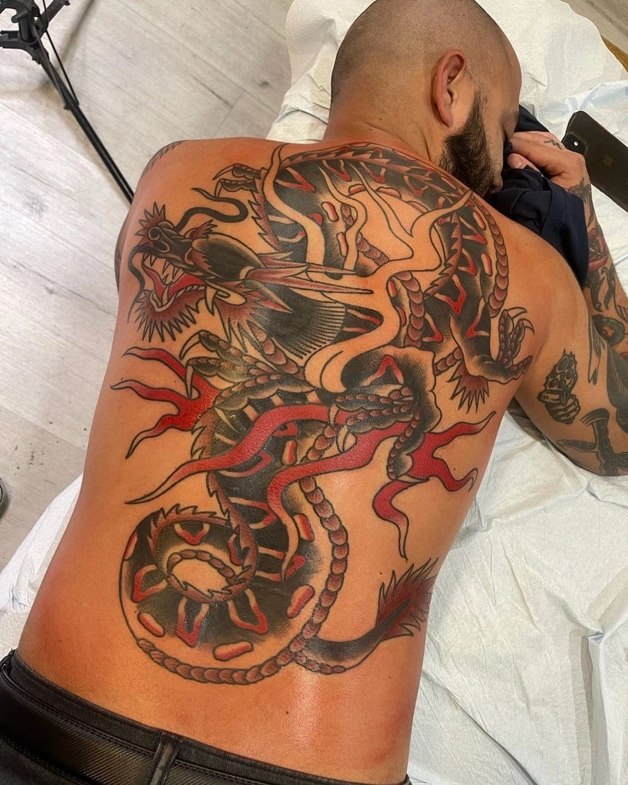 Neo-traditional tattoo of a large curling dragon with red accents covering a back