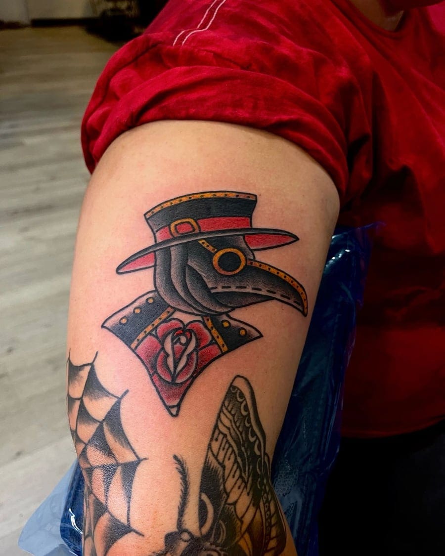 Neo-traditional upper arm tattoo of a plague doctor mask with a rose