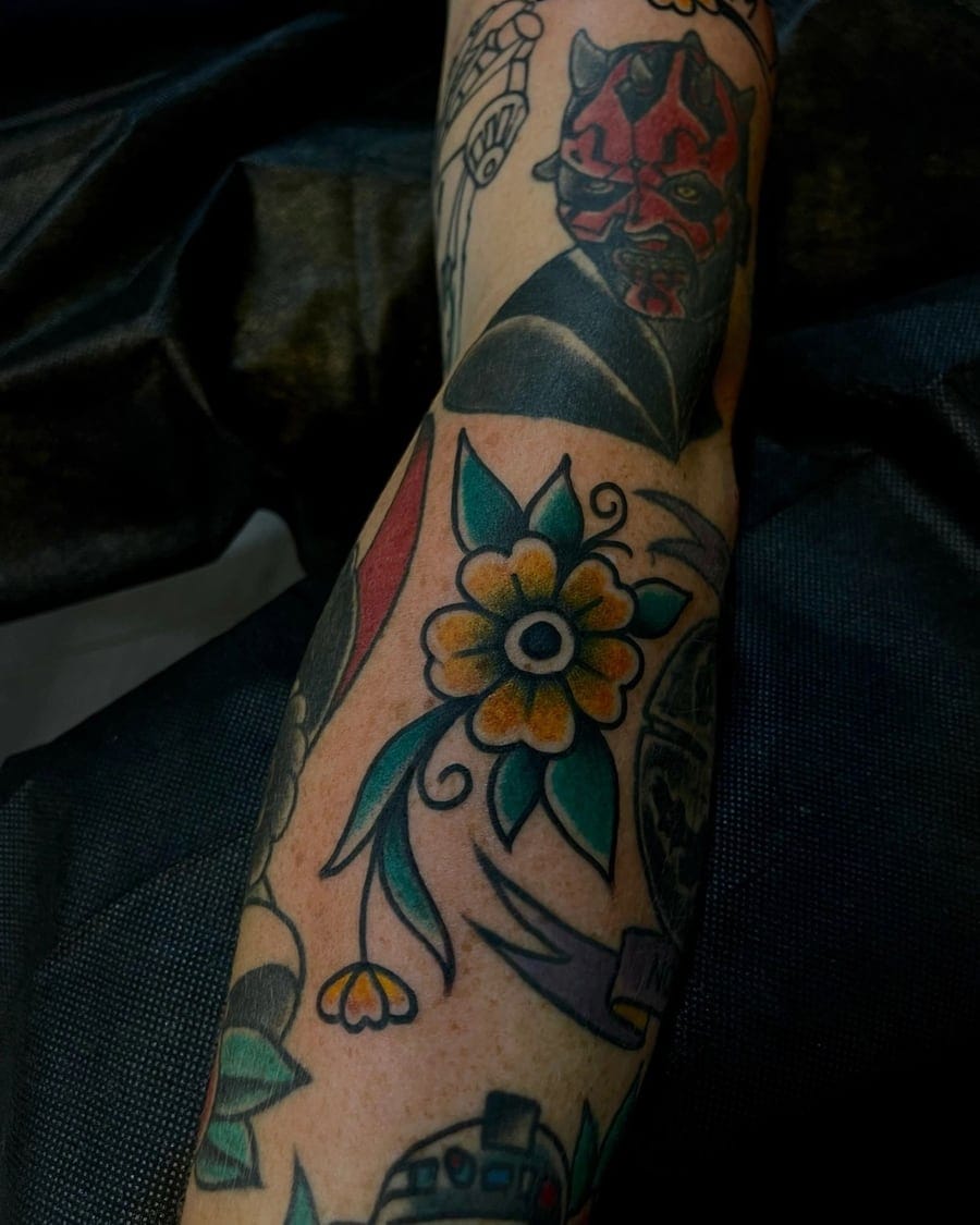 Neo-traditional forearm tattoo of a red devil face surrounded by floral and geometric designs