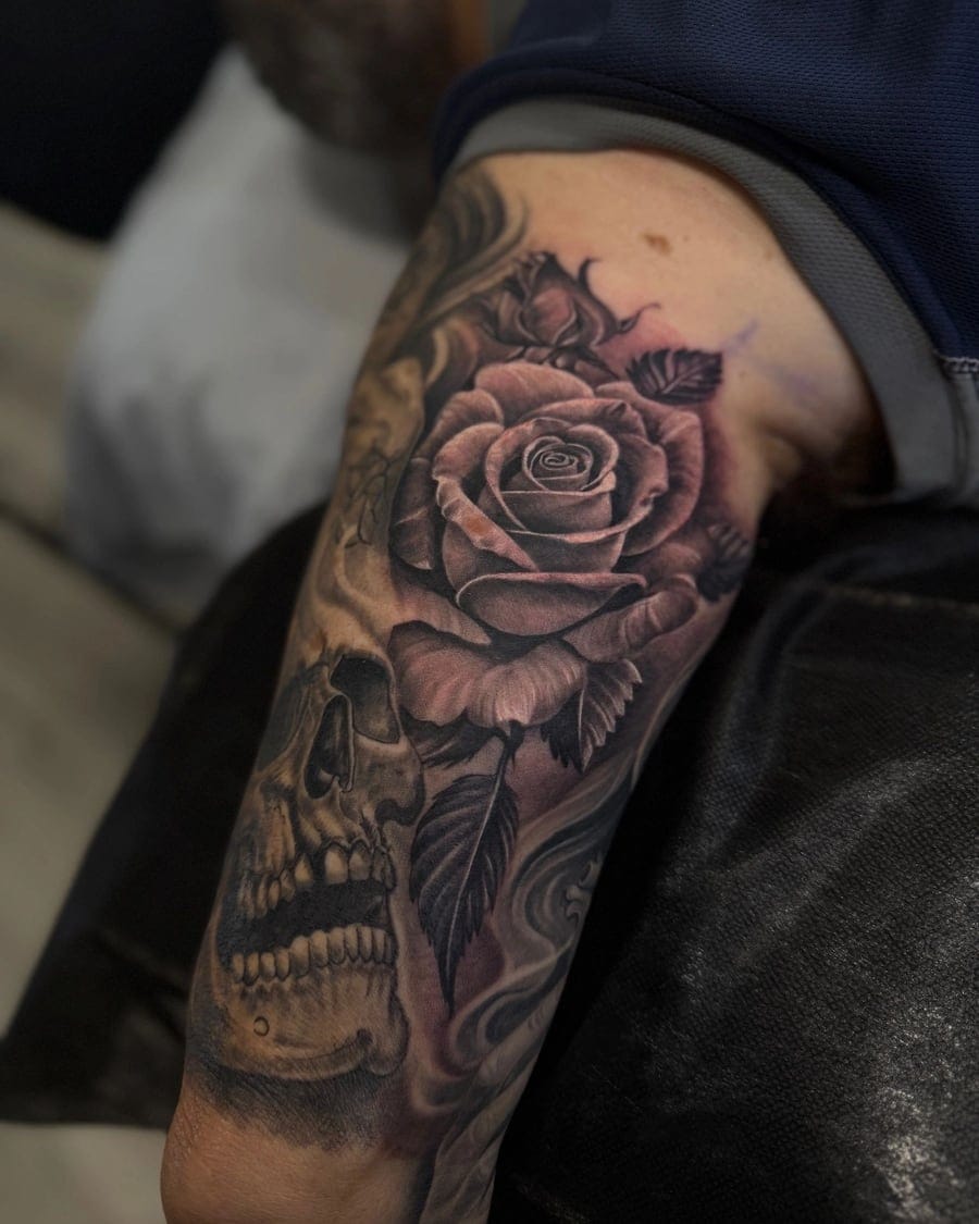 Black and grey forearm tattoo of a shaded rose above a skull with smoke detail